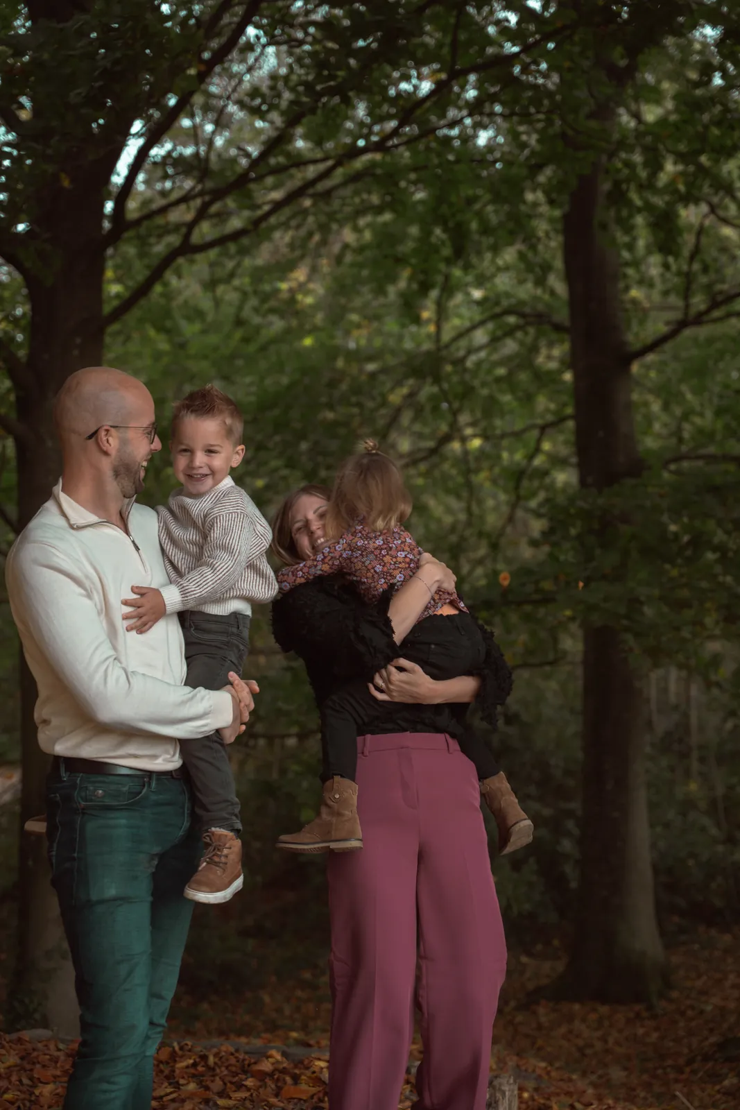 Gezinsshoot: ouders tillen hun kinderen lachend op in het bos
