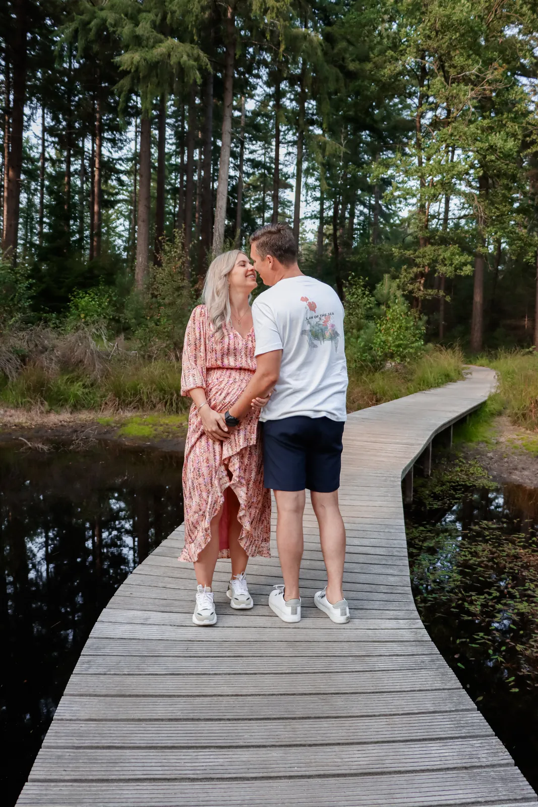 Zwangerschapsshoot: stel kust elkaar op een vlonderpad in het bos